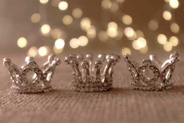 Happy Epiphany day concept. Three silver crowns, symbol of Tres Reyes Magos (Three Wise Men) on beige bokeh background.