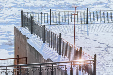 The railing of the fence of the embankment of the river in the snowy winter. Sunny day. No people. View from above