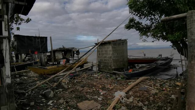 Typhoon-wrecked bamboo shanty houses made of light materials and wooden boats at the side of a high-tide lake.