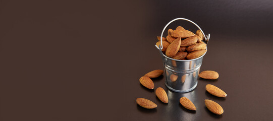 A small metal bucket filled with dried almond kernels on a black background.