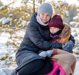 Fototapeta na wymiar Mother and daughter are sitting on a sleigh in the winter forest on Christmas holidays. Active winter holidays with children on winter holidays.