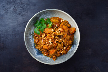 Traditional Indian vegetarian Madras curry stew with sweet potatoes and roasted cashew nuts served as top view in a grey Nordic design bowl with copy space