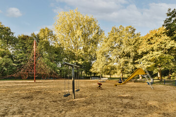 a playground with swings, slides and slides on the ground in front of trees that are turning to...