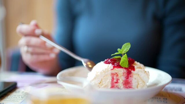 Close-up dessert on restaurant table, cake or cheesecake with berries. Girl holds spoon in hand, breaks off piece and tastes it, eating. Beauty serving of dish. Delicious food and sweetness. Tasting.