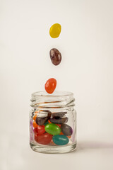falling colorful jelly beans dropping into a glass screw top jar isolated on a white background