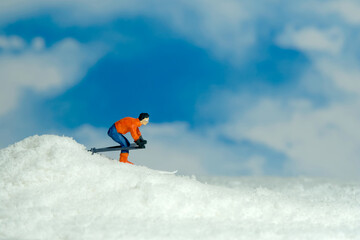 Miniature people toy figure photography. Winter sport. A male downhill ski racer slides down from the top of the hill.