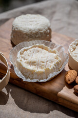 French cheeses Rocamadour and Saint-Marcellin served on olive tree wooden plank with almonds
