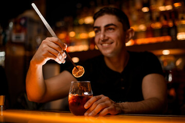 bartender holds slice of dry citrus with tweezers over glass with cold cocktail