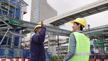 Structural engineers and construction workers are holding blueprints inspecting structure. sky train track construction in city. Blue collar wears a safety hardhat while working on construction site.