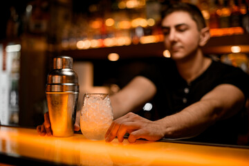 view on shaker and glass with ice and hands of bartender on bar counter