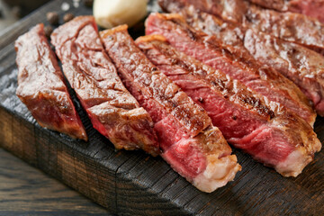 Steaks. Sliced grilled meat steak New York or Ribeye with spices rosemary and pepper on black marble board on old wooden background. Top view. Mock up.