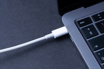 Charging battery laptop. Modern USB C port for fast charge. White cable plugged in laptop close-up...