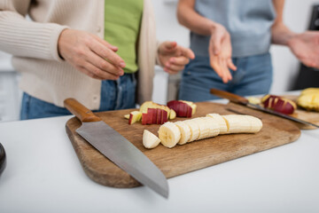 Cropped view of ripe fruits on cutting boards near blurred women in kitchen