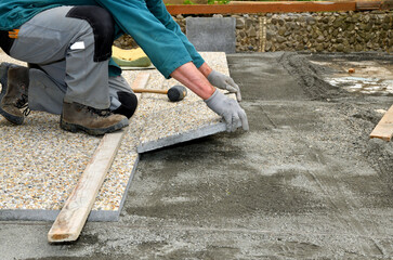 Paver on the knee lays concrete paving stone on the sidewalk 
