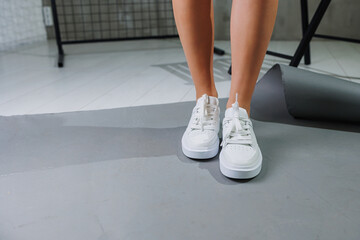 Beautiful woman in youth leather white sneakers and standing on white background. Women's legs with fashionable shoes. Casual white women's shoes