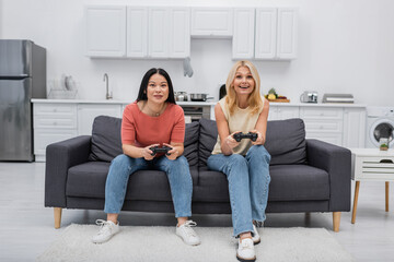 KYIV, UKRAINE - DECEMBER 2, 2021: Cheerful interracial friends playing video game at home