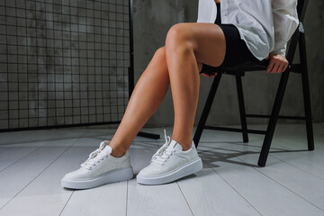 Beautiful female legs in leather white casual sneakers. Women's legs with fashionable shoes. Casual white women's shoes