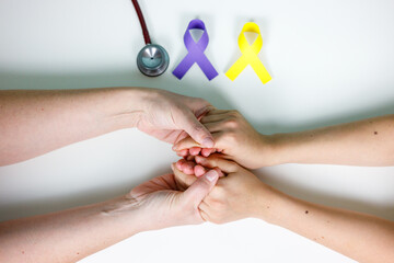 Adult's hands intertwined with a child's hands next to a stethoscope and yellow and purple ribbons, world cancer day concept