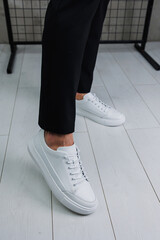 Close-up of male legs in black pants and white casual classic sneakers. Men's summer leather shoes