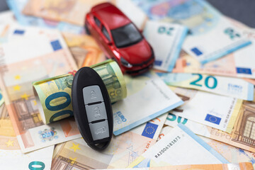 key and red toy car on pile of euro bills, buy or sell a car, rent a car or insurance concept.