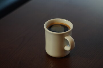 Hot americano coffee in a white mug placed on a wooden table.