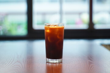 Cafe interior with window view and Ice Americano with cool ice on wooden table.