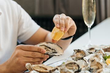A man's hands squeezes fresh lemon juice onto an raw opened oyster, lifestyle food, ready to eat. Oyster dinner with champagne in restaurant