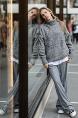 Obraz premium full length of young woman in grey outfit leaning on glass window display in New York