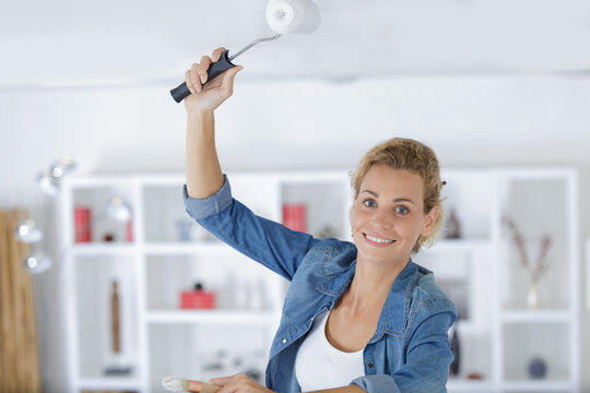 woman paints ceiling with brush at home