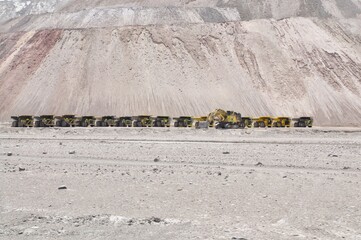 Huge mining trucks are parked in a row in front of a big hill. Mining trucks in Atacama desert,...