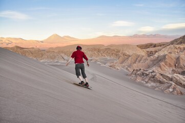 Sandboarding during sunset in Atacama desert, chile. A guy on a snowboard riding down a dune. Sandboarding in the 'Valle de la Luna', the valley of the Moon in Atacama desert, Chile. Guy in red shirt.