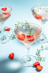 Glasses with cold pink champagne or punch with wine strawberries, ice and rosemary on blue background