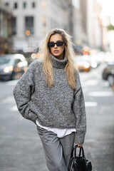 Obraz premium blonde woman in knitted sweater and sunglasses standing with trendy handbag on blurred street in New York