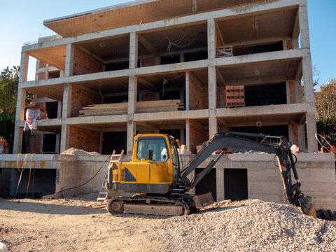 House construction site with small excavator in front of it facade view