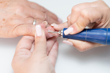 Manicurist scraping a senior woman's fingernail cuticle with a nail buffer