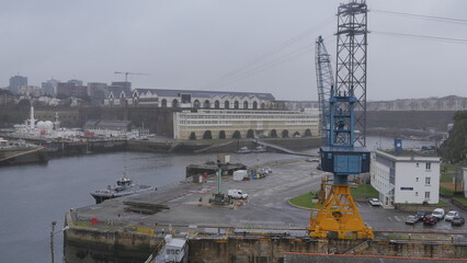 L'arsenal de Brest et tout l'équipement militaire et maritime, base militaire en plein milieu de la ville, sous un ciel nuageux et gris, pluvieux, des bateaux accostés dans l'eau ou dans le fleuve,