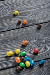 Chocolate candy in multi-colored glaze. Scattered on black pine boards.