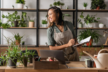 cheerful african american florist with notebook looking away near laptop and potted plants in flower shop © LIGHTFIELD STUDIOS