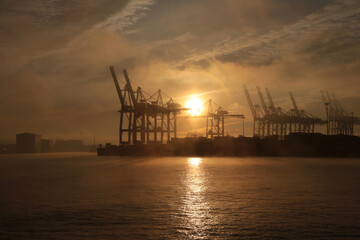 Naklejka na ściany i meble Dramatischer Sonnenaufgang über den Hamburger Hafen mit Nebel und Wolken im Winter 