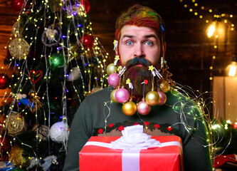 Christmas beard decorations. Surprised bearded man with present gift box. New Year holidays.