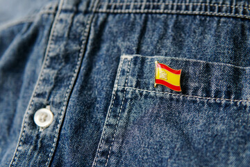 Metal badge with the flag of Spain is pinned on blue jeans jacket. Spain patriotism concept. Independence Day Holiday in Spain.