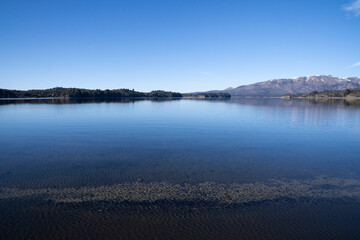 View of the lake, forest and mountains in a sunny day with a deep blue sky. 