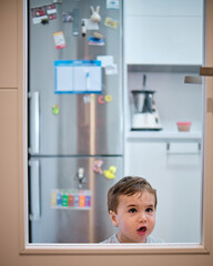 Fototapeta na wymiar Toddler playing behind the glass of the kitchen door. Angry gesture