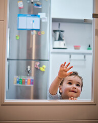 Toddler playing behind the glass of the kitchen door. Leaning his hands on the glass