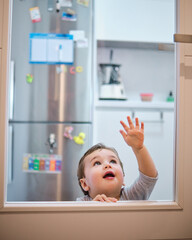 Toddler playing behind the glass of the kitchen door. Leaning his hands on the glass