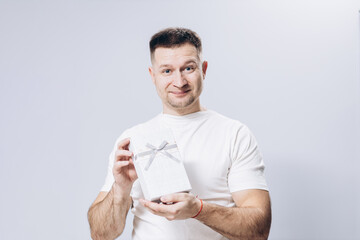 A man in a white t-shirt holds a birthday and valentine's day gift in his hand