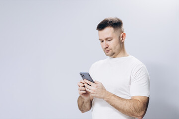 A man in a white T-shirt holds a mobile phone in his hand. Attractive guy