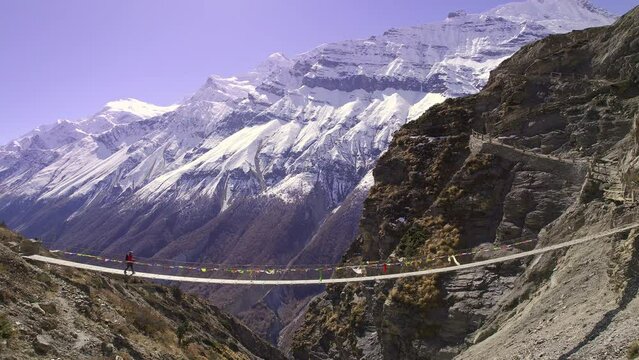 Person walking over bridge through the Himalaya mountains in Nepal viewing snow  on the peaks.