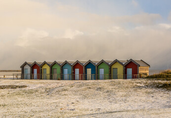 Fototapeta na wymiar The colorful beach huts at Blyth beach surrounded by snow in a wintery Northumberland, England