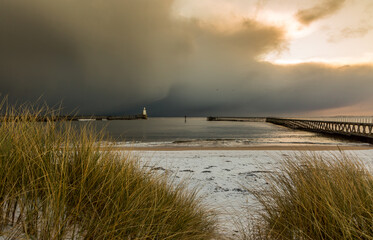 A freezing, snowy morning at Blyth beach, looking across the sand dunes and marram grass towards the old wooden Pier